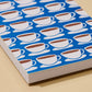 A close-up of a notebook or journal with a blue cover patterned with repeating white coffee cups and saucers, resting on a light beige surface.