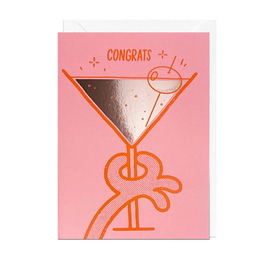 Pink greeting card with cartoon hand holding up a big martini glass with silver foil detail. Single cocktail olive on a pick rests inside. Text reads "Congrats."