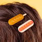 Corndog hair clip and hotdog hair clip being worn on brown hair.