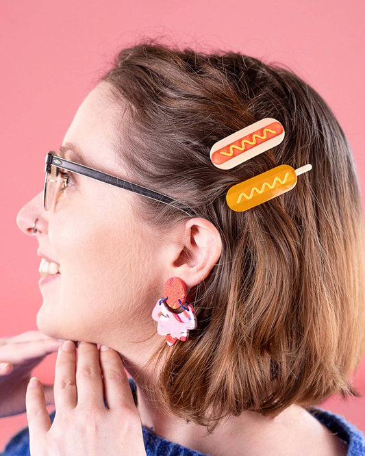 Woman in glasses wearing a corndog hair clip and a hotdog hair clip.