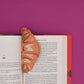 Bookmark shaped like a croissant shown inside an open book.