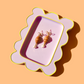 Pair of croissant earrings on a decorative pink and yellow tray against a peach background