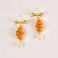 Pair of earrings with orange spiral designs and gold bows on a light background