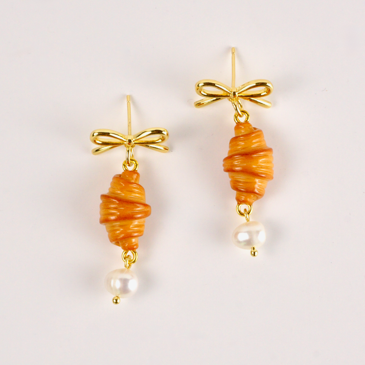Pair of earrings with orange spiral designs and gold bows on a light background