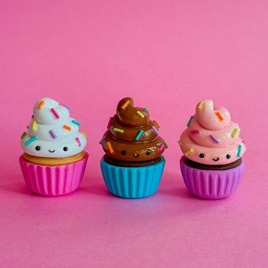 Three colorful cupcake-shaped items with faces on a pink background