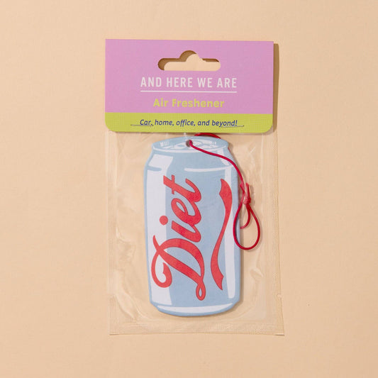 A Diet soda air freshener car fragrance shaped like a light blue soda can with red script lettering, sealed in a clear plastic bag with a pink and green header card that reads 'AND HERE WE ARE Diet freshener'.