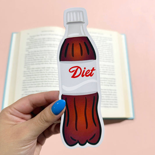 Hand holding a Diet Coke bottle-shaped bookmark with an open book in the background.