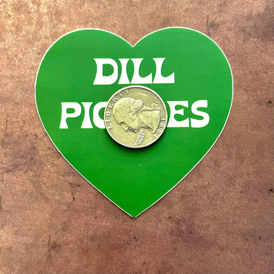 Green, heart shaped sticker with text in middle that reads "Dill Pickles"  with a quarter on top of it for scale 