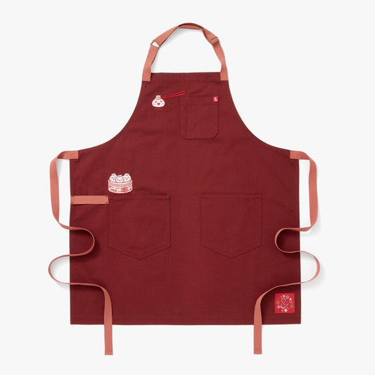 Cinnamon colored apron with mauve straps. This apron has a design that is dedicated to Dim Sum and has a steamer basket full of smiling dumplings and one dumpling being grabbed by chopsticks.