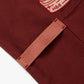 Cinnamon colored apron with mauve straps. This apron has a design that is dedicated to Dim Sum and has a steamer basket full of smiling dumplings and one dumpling being grabbed by chopsticks. This photo shows the detail of the towel loop.