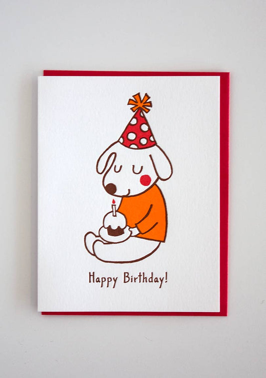 Card with a dog wearing a polkda dot party hat and a mustard colored sweater. Dog is holding a cupcake that has a candle in it. Text reads: Happy Birthday!