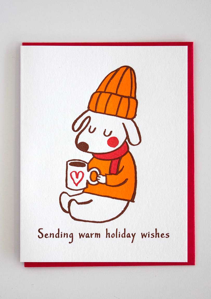 Dog wearing a mustard colored beanie and sweater with red scarf sitting with a cup of warm liquid. Text reads: Sending warm holiday wishes. Greeting card.