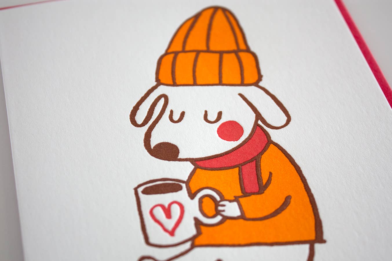 Dog wearing a mustard colored beanie and sweater with red scarf sitting with a cup of warm liquid. Text reads: Sending warm holiday wishes. Greeting card.