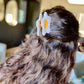 Girl with long brown hair wearing a fried egg hair clip.