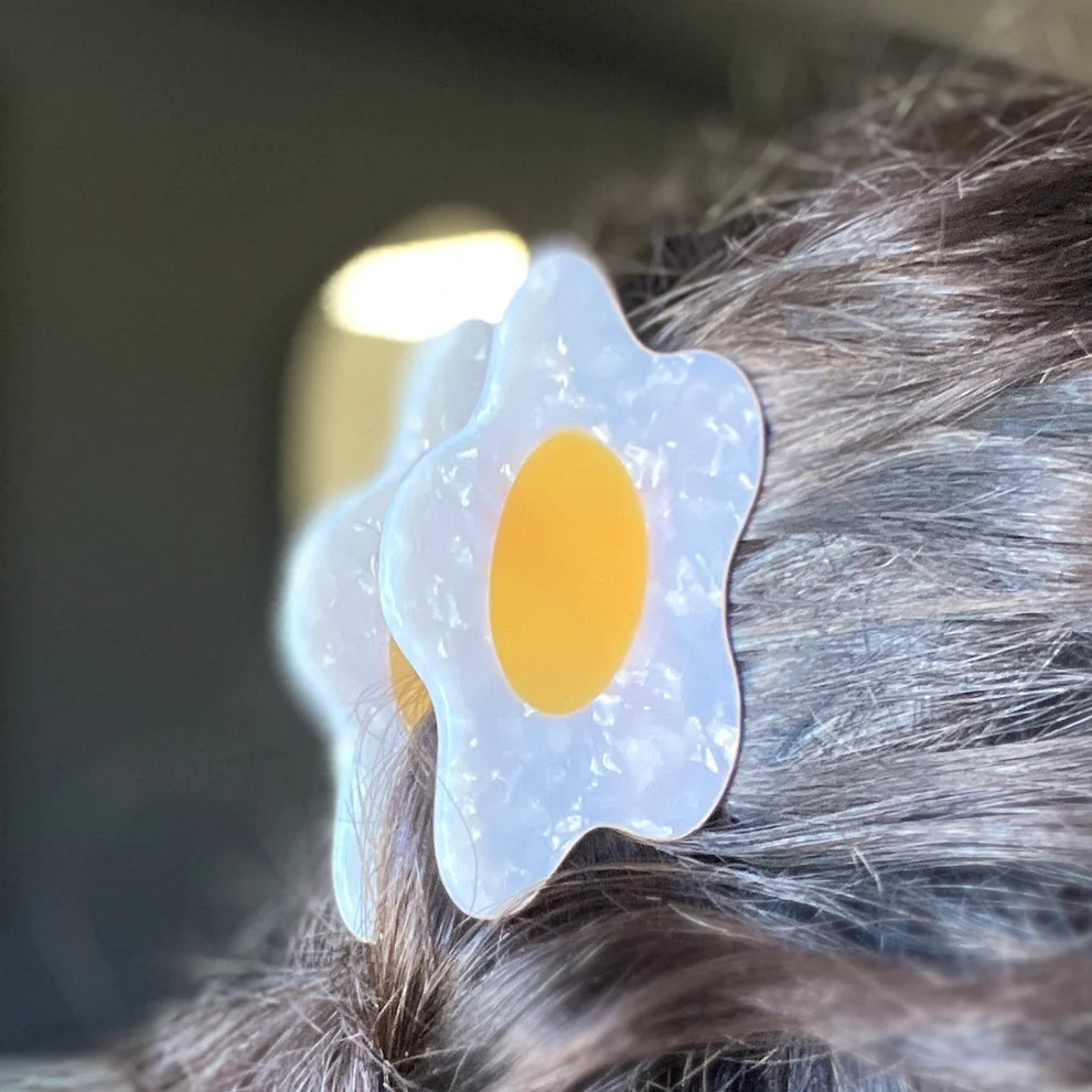 Girl with long brown hair wearing a fried egg hair clip.