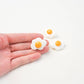 Three fried egg magnets in the picture and one is in the hand to show size and detail