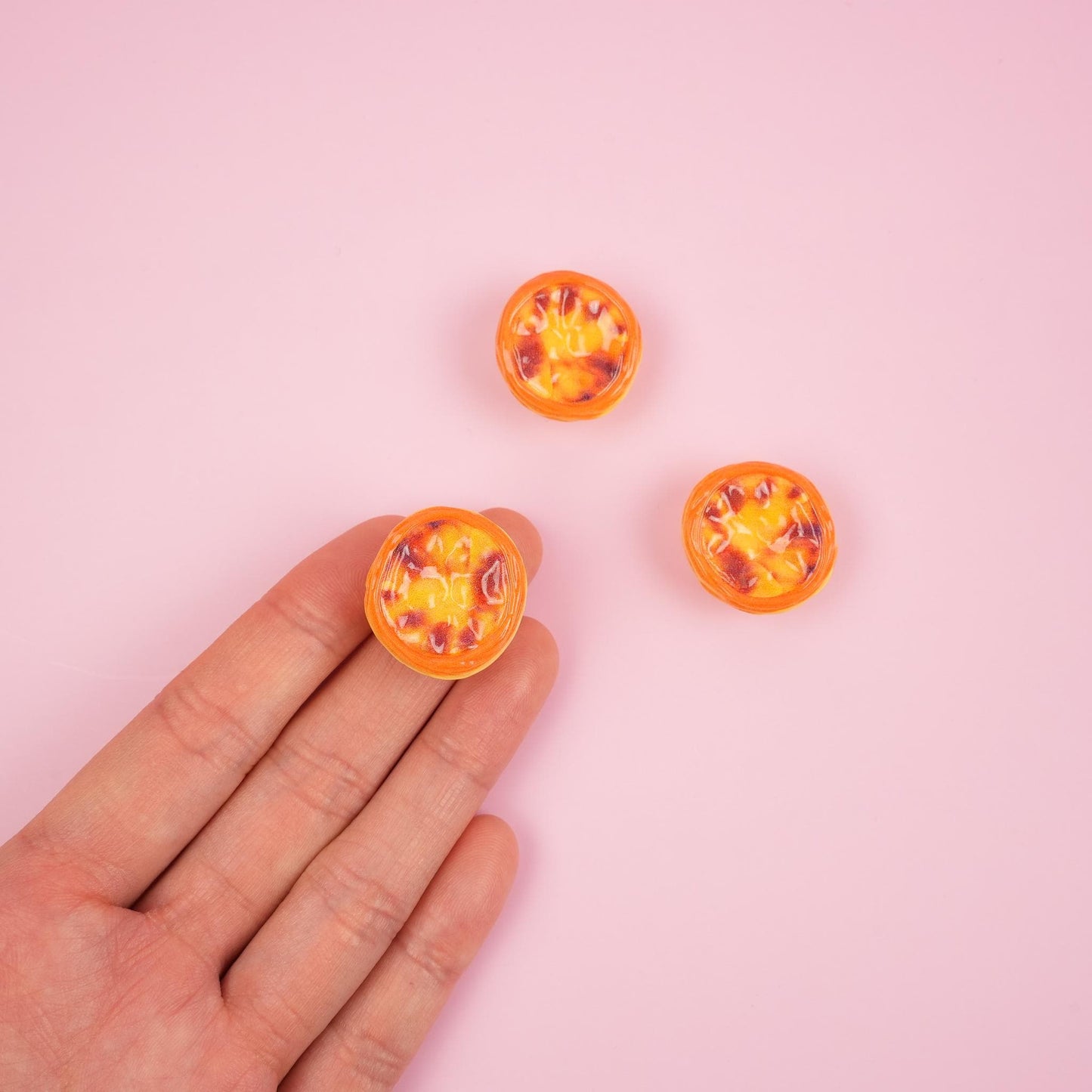 Three egg tart magnets and one is on a hand to display its size.