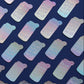 A repeating pattern of small rectangular stickers or labels with rounded corners, each printed with the phrase “Emotional Support Water Bottle” in white text over an iridescent pastel holographic finish. The stickers are arranged diagonally on a dark navy blue background.