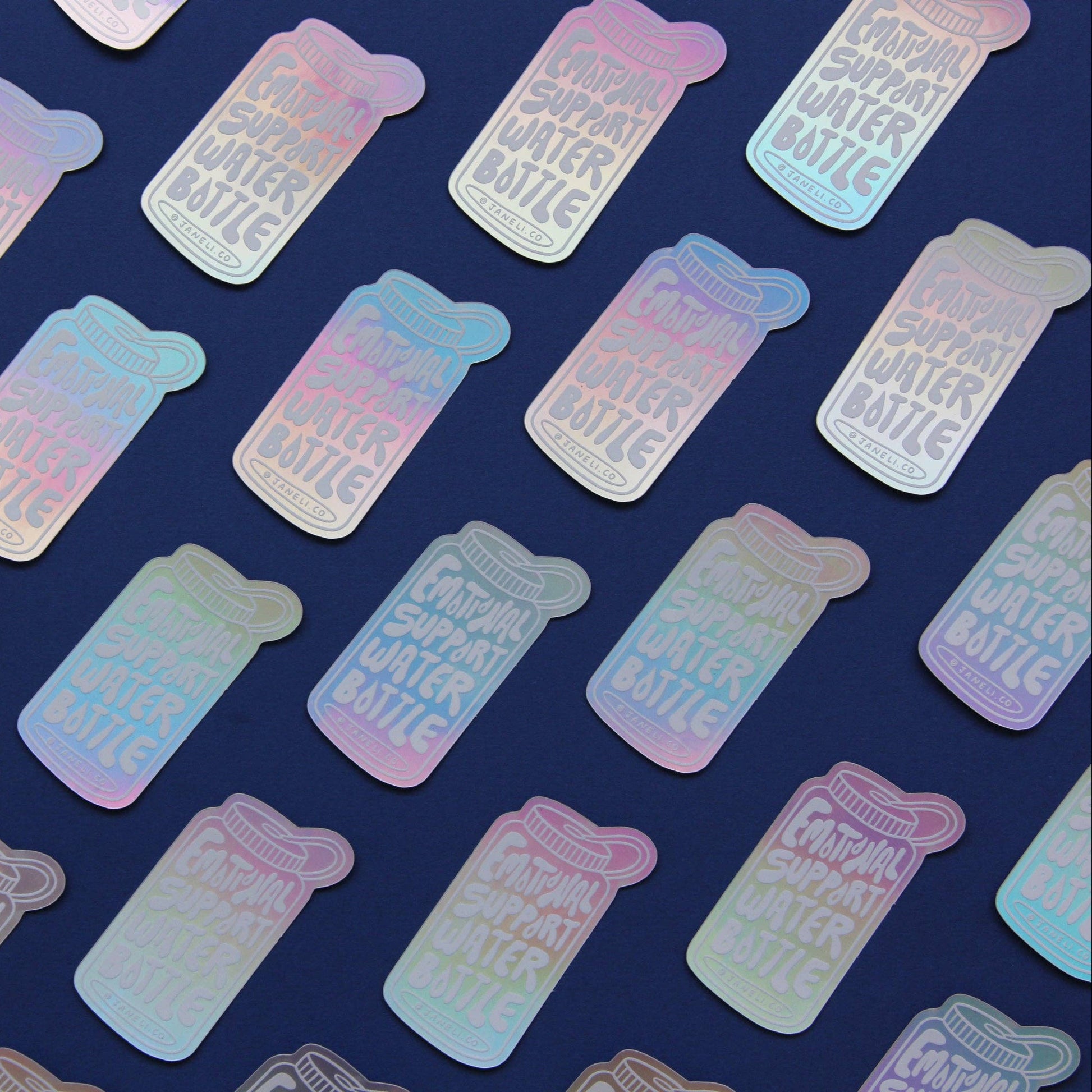 A repeating pattern of small rectangular stickers or labels with rounded corners, each printed with the phrase “Emotional Support Water Bottle” in white text over an iridescent pastel holographic finish. The stickers are arranged diagonally on a dark navy blue background.
