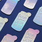 A repeating pattern of die-cut stickers shaped like a water bottle, featuring the text 'EMOTIONAL SUPPORT WATER BOTTLE' in a light gray font over an iridescent pastel gradient background. The stickers are arranged diagonally on a dark navy blue surface.