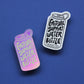 Two stickers shaped like water bottles on a solid blue background. One is holographic pink and purple with the text 'EMOTIONAL SUPPORT WATER BOTTLE' in light pink.