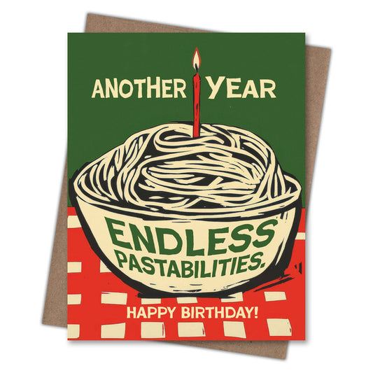 A novelty birthday card featuring a retro-style illustration of spaghetti in a bowl with a single lit candle, set against a dark green background with the text 'ANOTHER YEAR ENDLESS PASTABILITIES. HAPPY BIRTHDAY!'.
