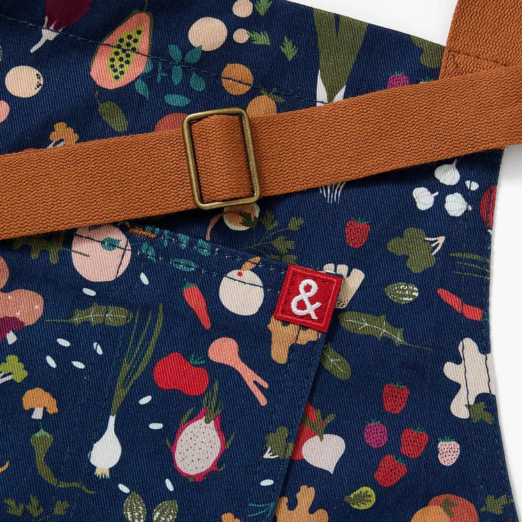 Close up of dark blue apron with a design pattern of a variety of colorful produce with brown neck and waist straps