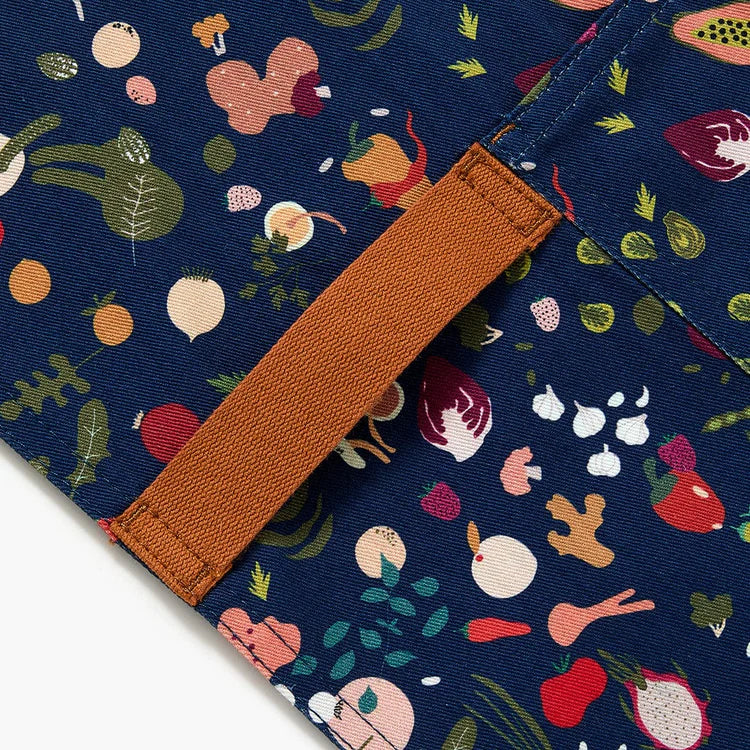 Close up of dark blue apron with a design pattern of a variety of colorful produce with brown neck and waist straps