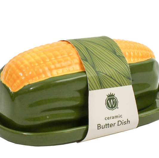 A ceramic butter dish shaped like a corn cob, featuring a glossy dark green base and a bright yellow-orange corn tip, wrapped in a paper band with the brand name 'W' and 'ceramic Butter Dish' printed on it.