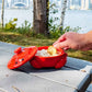 Red crab-shaped container with food on a wooden surface by a waterfront