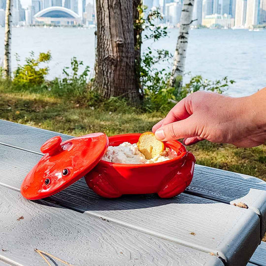 Red crab-shaped container with food on a wooden surface by a waterfront