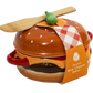 A ceramic brie cheese baker shaped like a hamburger, with a wooden spatula resting on top and a paper tag reading 'Ceramic Brie Cheese Baker' on a white background.