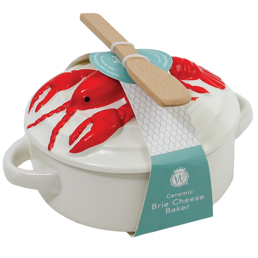 White ceramic Brie cheese baker with a lid decorated with red lobster illustrations, featuring a wooden spatula resting on top and a teal paper tag.