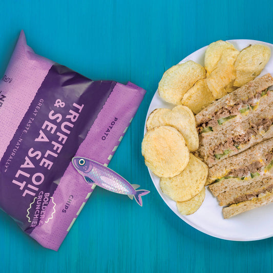 A plate with a sandwich and chips next to a bag of chips with a chip clip that looks like a purple fish.