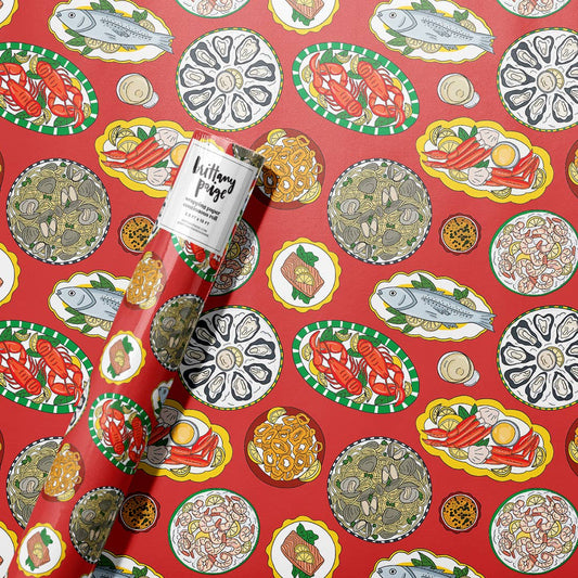A roll of wrapping paper featuring a red background with a colorful illustrated pattern of seafood dishes shown with the paper unrolled and a branded paper sleeve visible.