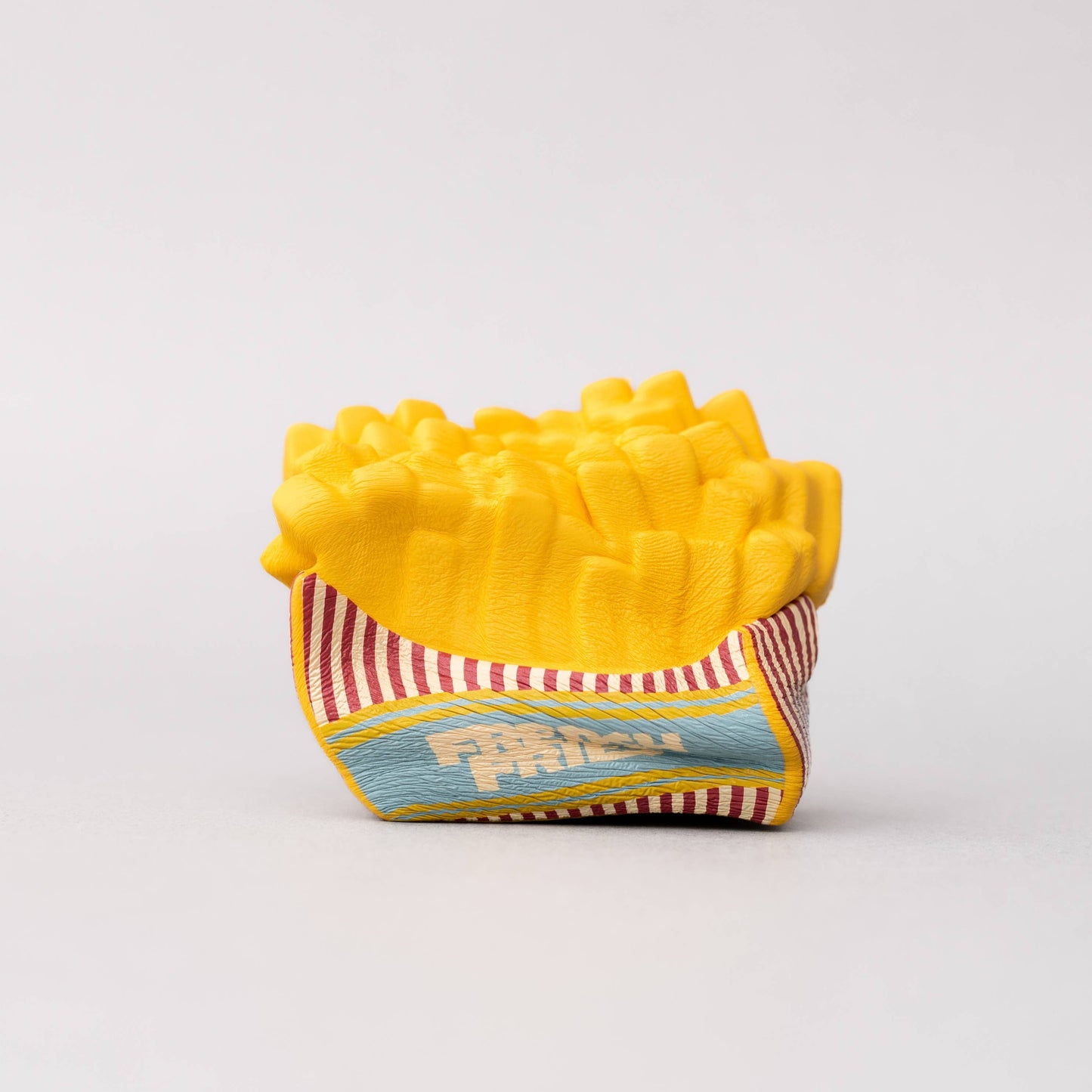 Yellow toy french fry container on a white background. Stress ball squished.