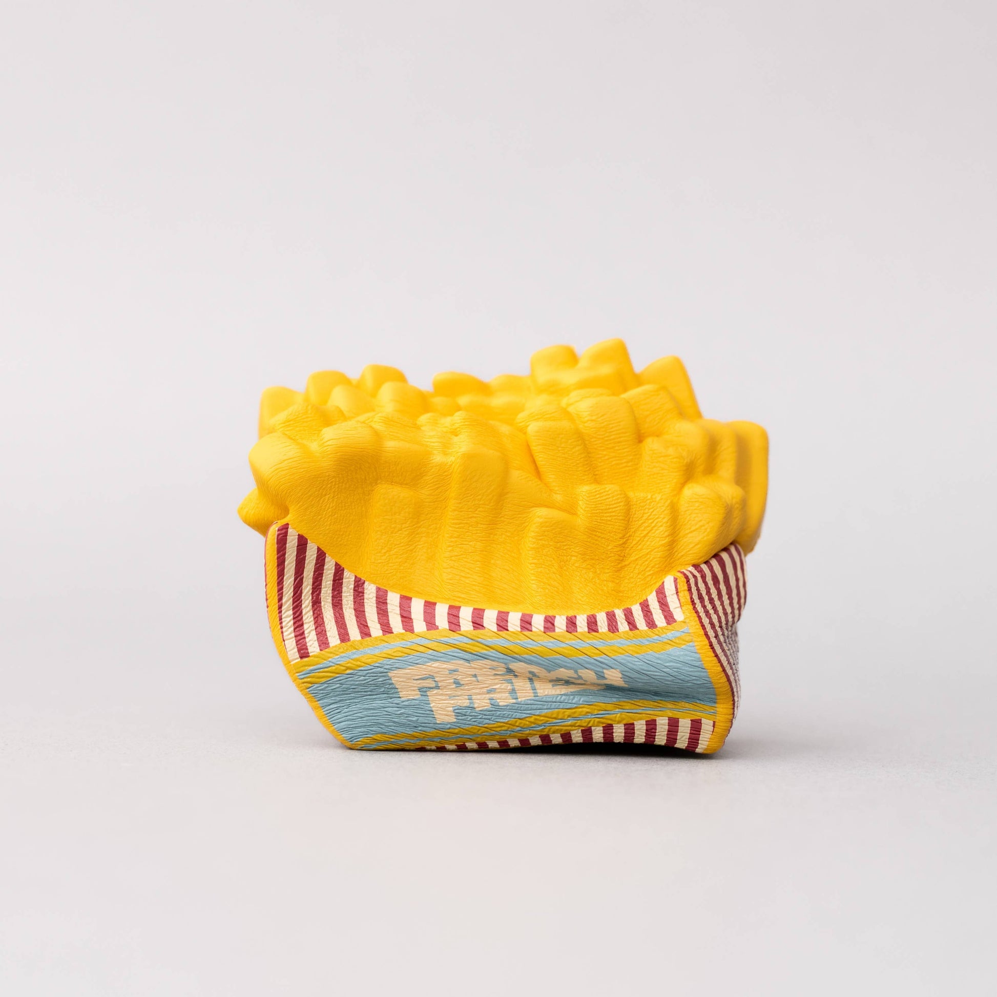 Yellow toy french fry container on a white background. Stress ball squished.