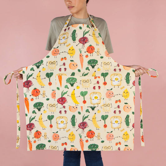 Person wearing a colorful apron with cartoon food characters on a pink background