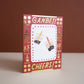 greeting card with gold foil text and symbols around the border. Center has illustrations of two boba cups. Text up top reads "Ganbei!" which is a form of "cheers" or "bottoms up" in Chinese. Bottom text reads "Cheers!" 