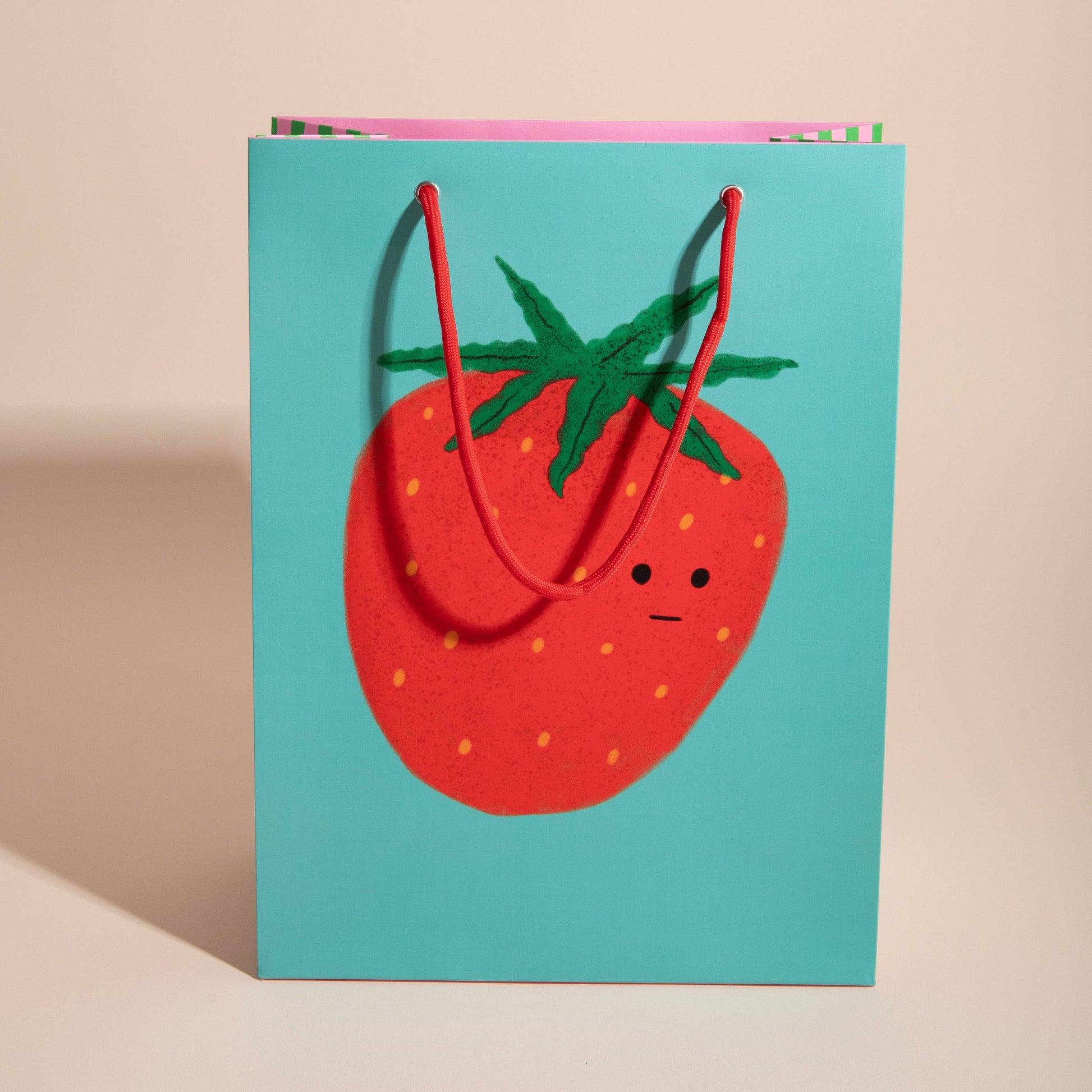 gift bag with a single giant strawberry on a turquoise background