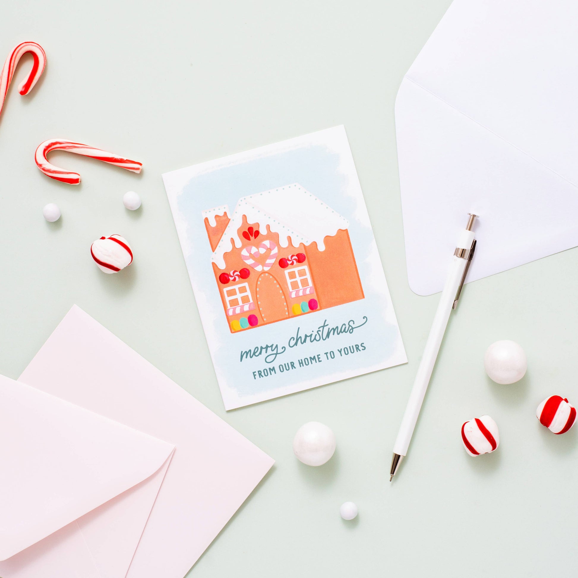 Holiday greeting card with a decorated gingerbread house on it. Text at bottom reads "Merry Christmas from our home to yours" 