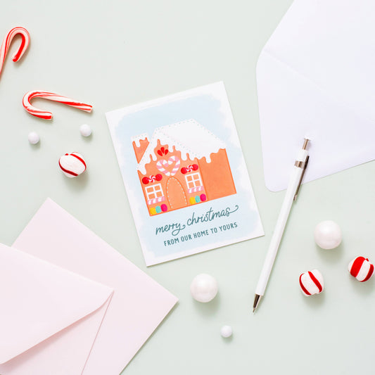 Holiday greeting card with a decorated gingerbread house on it. Text at bottom reads "Merry Christmas from our home to yours" 