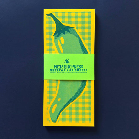 Notepad with green and yellow checkered design and 'Pier Six Press' branding on a dark blue background