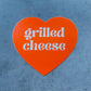 Orange heart shaped sticker with text that reads: Grilled Cheese