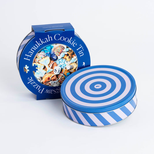 Round cookie tin that is blue and white stripe. Outer cover says Hanukkah Cookie Tin Jigsaw Puzzle with a photo of traditional cookies and dreidel. 