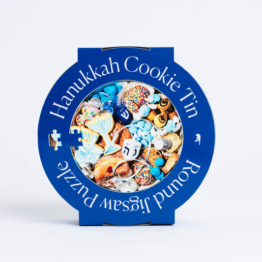 Round cookie tin that is blue and white stripe. Outer cover says Hanukkah Cookie Tin Jigsaw Puzzle with a photo of traditional cookies and dreidel. 