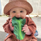 Photo of baby holding kale toy in their hands.
