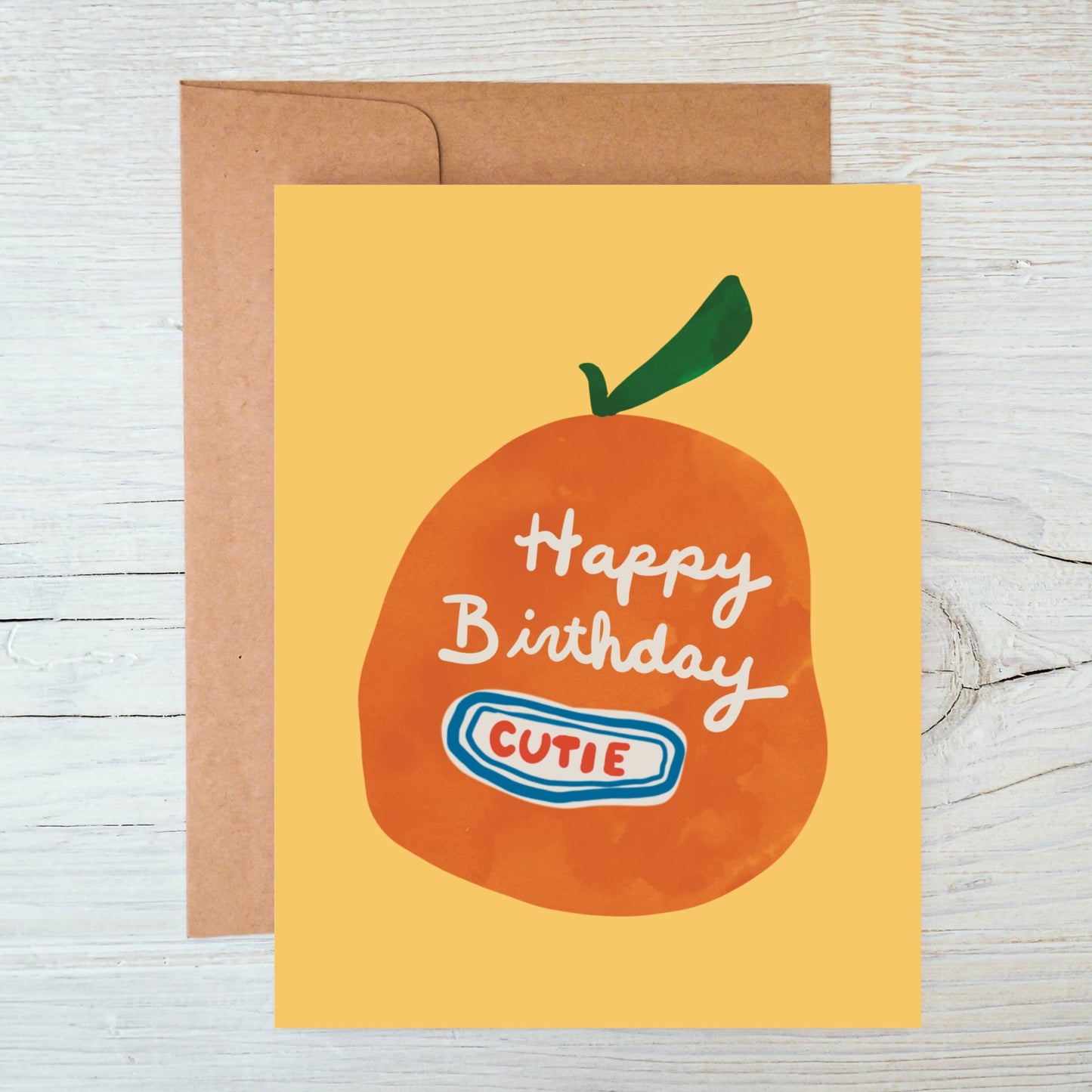 Birthday card with an orange and 'Happy Birthday Cutie' text on a yellow background, with a brown envelope.