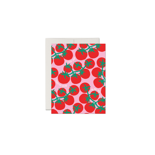 A greeting card with a repeating pattern of red tomatoes on a light pink background, shown with a white envelope behind it on a plain white background.