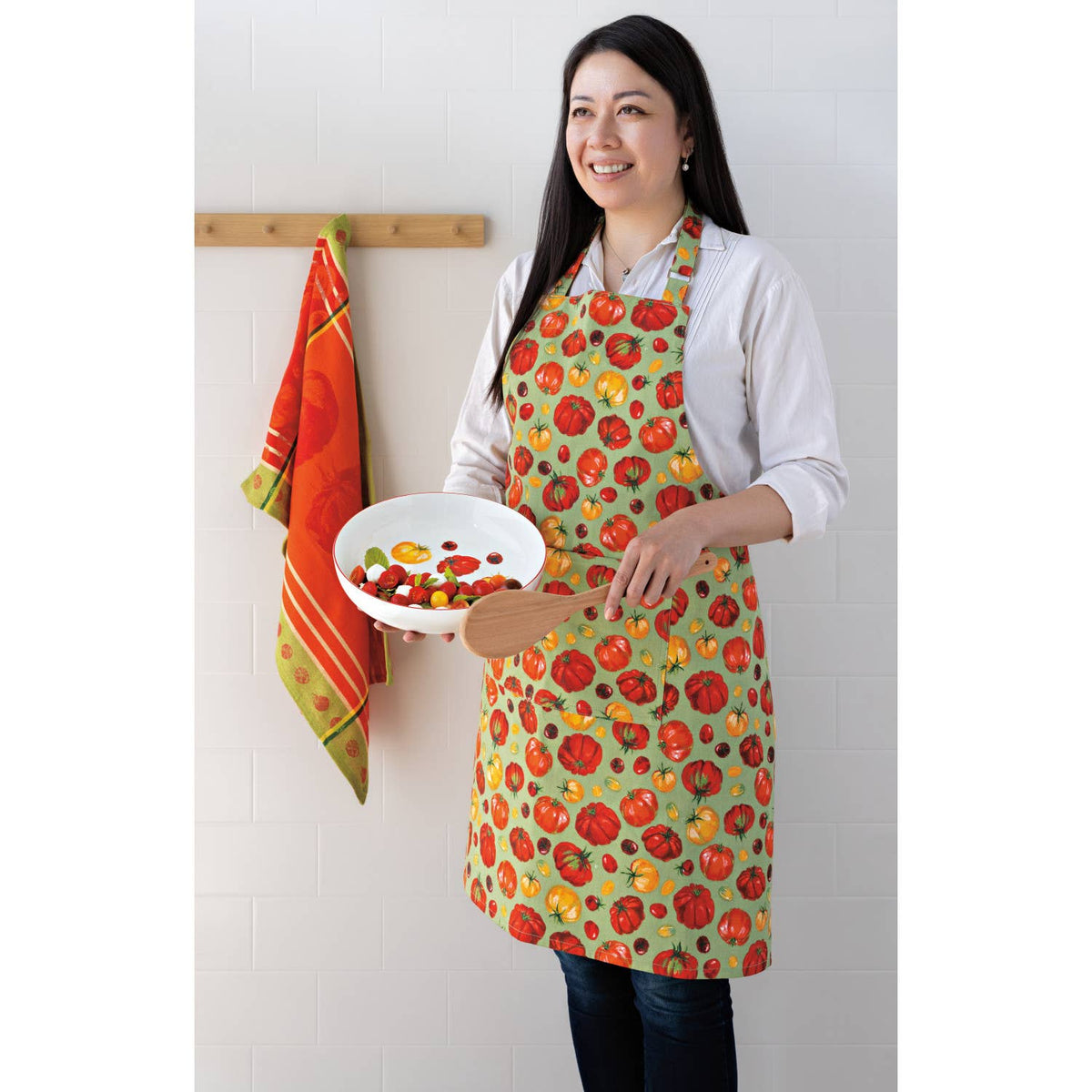 Woman wearing a colorful apron holding a plate of food in a kitchen setting.
